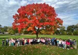 Kinder students standing in from of a fall tree